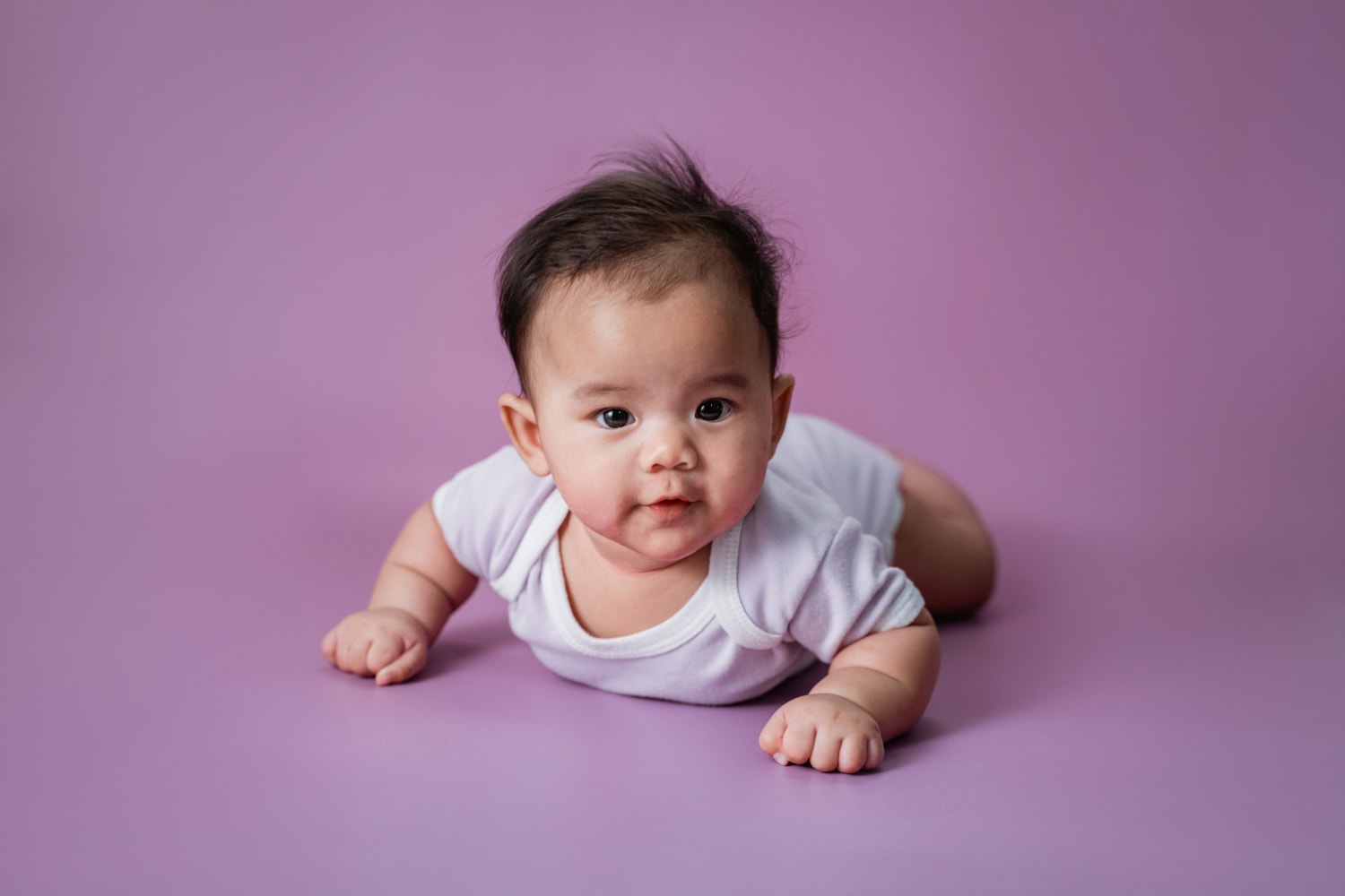 Baby liggend op de buik met paarse achtergrond