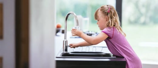 Meisje dat glas vult met water uit de kraan