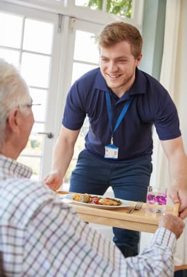 Verpleger geeft dienblad met eten aan oudere man