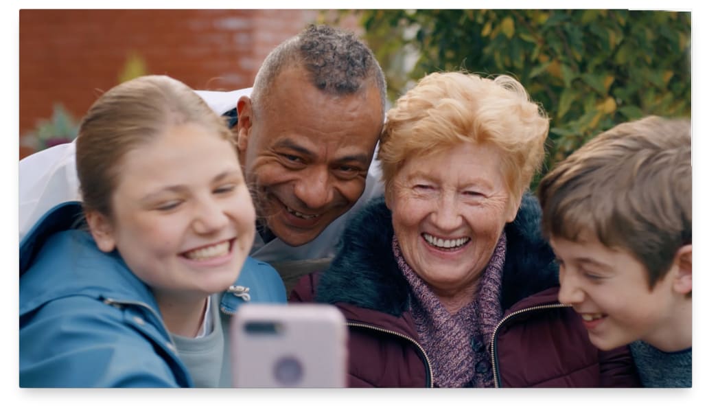 Oma en twee kleinkinderen maken een selfie met een verpleegkundige erbij